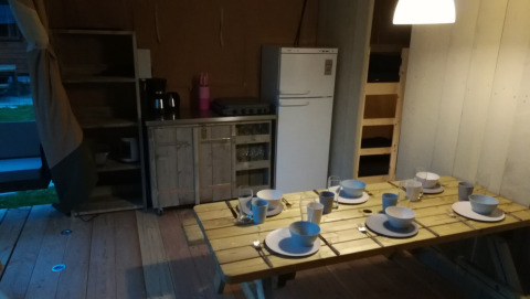 Comedor en una tienda Safari en Camping Val d'Or, Luxemburgo, con mesa puesta y pequeña cocina.