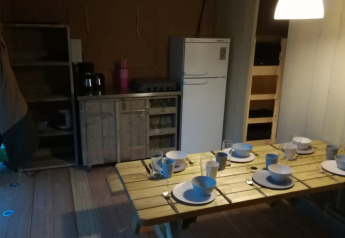 Essbereich im Safari-Zelt auf Camping Val d'Or, Luxemburg, mit gedecktem Tisch und Küchenzeile.