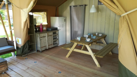 Interior de tienda safari en Camping Val d'Or, Luxemburgo, con mesa de comedor, cocina y nevera.
