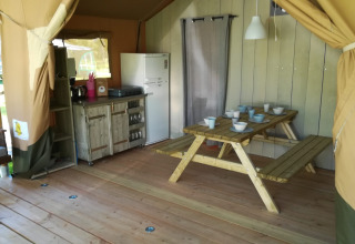 Interior de tienda safari en Camping Val d'Or, Luxemburgo, con mesa de comedor, cocina y nevera.
