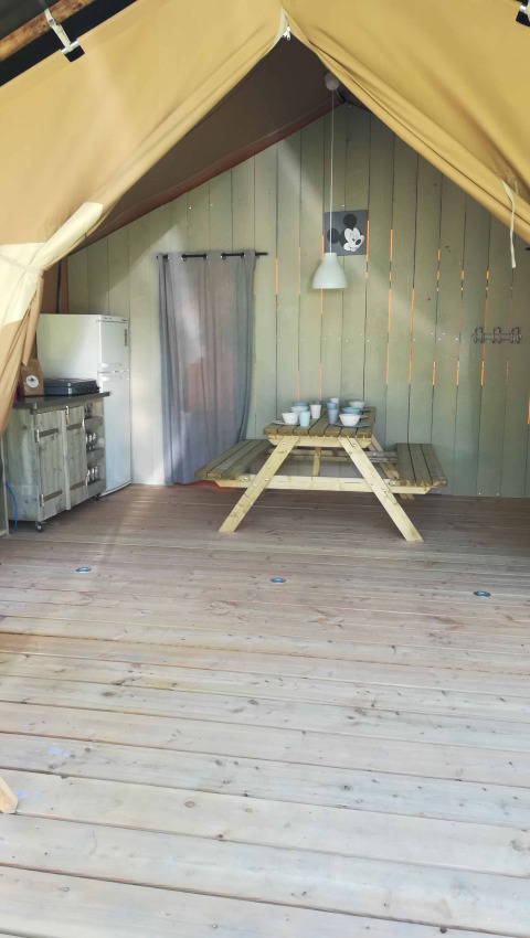 Inside a safari tent lodge at Camping Val d'Or in Luxembourg, featuring a wooden table, kitchen, and fridge.
