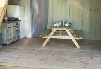 Inside a safari tent lodge at Camping Val d'Or in Luxembourg, featuring a wooden table, kitchen, and fridge.
