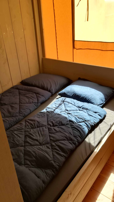 Interior view of a Safari tent lodge at Camping Val d'Or, showing two single beds with blue bedding.