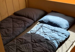 Interior view of a Safari tent lodge at Camping Val d'Or, showing two single beds with blue bedding.