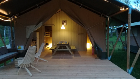 Tente safari au Camping Val d'Or au Luxembourg avec terrasse en bois, table, chaises et éclairage doux.