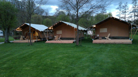 Tres tiendas safari en Camping Val d'Or en Luxemburgo, rodeadas de césped verde y árboles al anochecer.