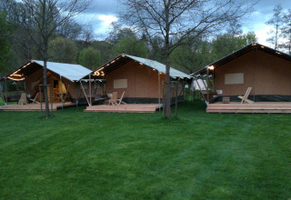 Tres tiendas safari en Camping Val d'Or en Luxemburgo, rodeadas de césped verde y árboles al anochecer.