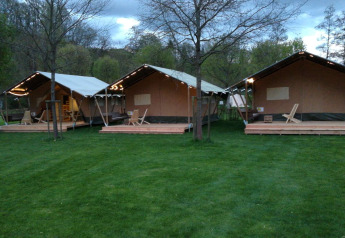 Three safari tents at Camping Val d'Or in Luxembourg, set on green grass with trees at dusk.