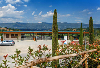 Vakantiepark in Toscane, Italië met hoofdgebouw, parking, cipressen en heuvelachtige achtergrond onder blauwe lucht.