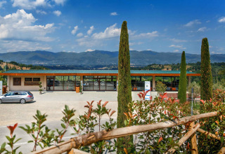Holiday park in Tuscany, Italy with a reception building, car park, cypress trees, and rolling hills in the background.