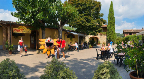 Familias y niños en el hu Norcenni Girasole Village en la Toscana, Italia, junto a una mascota y mesas al aire libre.
