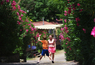 Una mujer y un niño caminan por un sendero rodeado de flores rosas en hu Norcenni Girasole Village, Toscana, Italia.