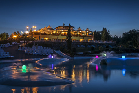 Avondzicht op hu Norcenni Girasole Village vakantiepark in Toscane met verlichte zwembaden en gebouwen.