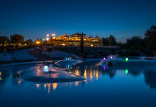 Vista serale di hu Norcenni Girasole Village in Toscana, Italia, con piscina illuminata e sedie sdraio.
