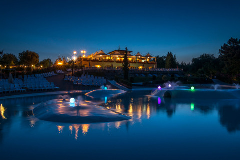 Imagen nocturna de hu Norcenni Girasole Village en la Toscana, Italia, con piscina iluminada al aire libre.
