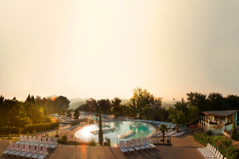 Amanecer sobre piscina con tumbonas, árboles y ambiente relajante en un parque vacacional en Toscana, Italia.