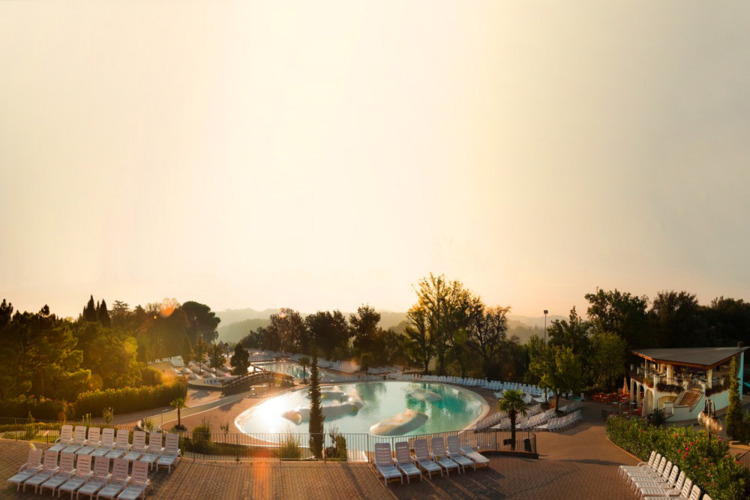 Lever de soleil sur une piscine avec chaises longues, arbres et ambiance paisible à un parc en Toscane, Italie.