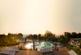 Solopgang over poolområde med liggestole, træer og afslappende omgivelser i en feriepark i Toscana, Italien.