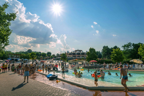 Holiday park in Tuscany with families enjoying the outdoor pool and sunshine on a bright summer day.
