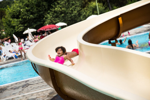 Child in pink swimsuit sliding down a waterslide at Norcenni Girasole Village holiday park in Tuscany, Italy.