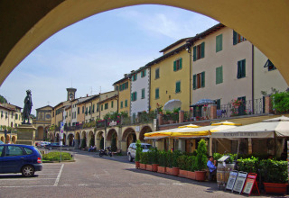 Foto van een gezellig Toscaans dorpsplein in Italië met terrassen, beelden en kleurrijke gebouwen.