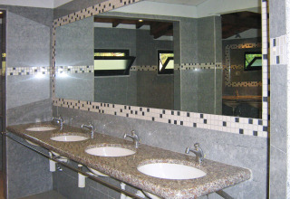 Moderne publieke badkamer met vier lavabo’s, granieten blad en grote spiegels in Norcenni Girasole Village.