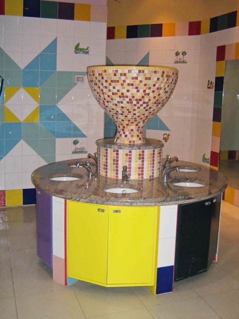 Colorida zona de lavabos con azulejos de mosaico y grandes cuencos en un baño público en Italia.