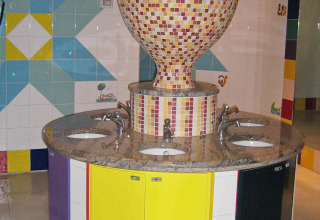 Colorful sink area with mosaic tiles and large communal basins in a public bathroom at an Italian holiday park.