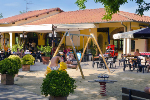 Cafetería al aire libre y parque infantil en un resort vacacional en la Toscana, Italia, con familias.