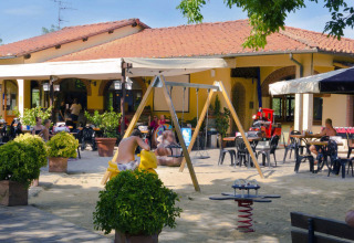 Udendørs cafeområde med legeplads til børn, folk sidder og slapper af i solen, Toscana, Italien.