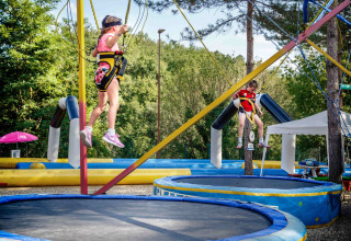 Kinderen springen op trampolines met veiligheidsgordels in een vakantiepark in Toscane, Italië.
