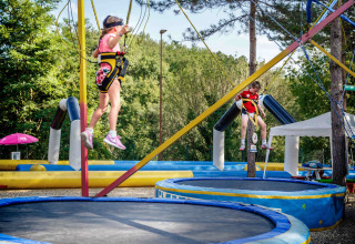 Bambini saltano sui trampolini con imbracature in un parco vacanze all’aperto in Toscana, Italia.