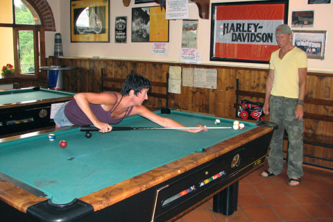 Two people playing pool at hu Norcenni Girasole Village holiday park in Tuscany, Italy, near a Harley-Davidson sign.