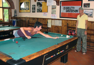 Two people playing pool at hu Norcenni Girasole Village holiday park in Tuscany, Italy, near a Harley-Davidson sign.