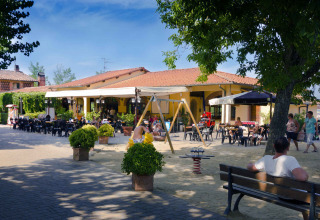 Outdoor dining area and playground with people at hu Norcenni Girasole Village holiday park in Tuscany, Italy.