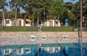 View of the pool and holiday cottages surrounded by pine trees at Camping Village Mare Pineta, Italy.