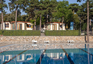 Udsigt over swimmingpool og ferieboliger omgivet af fyrretræer på Camping Village Mare Pineta i Italien.