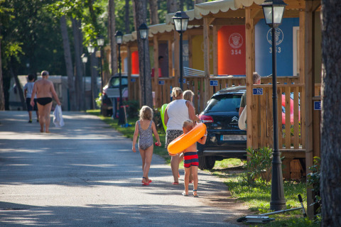 Familia paseando frente a cabañas de colores en Camping Village Mare Pineta, Friuli-Venezia Giulia, Italia.