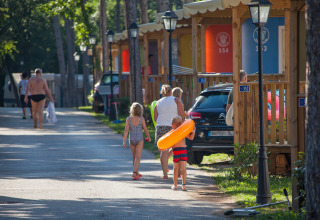 Familie går på vej foran farverige hytter i Camping Village Mare Pineta, Friuli-Venezia Giulia, Italien.