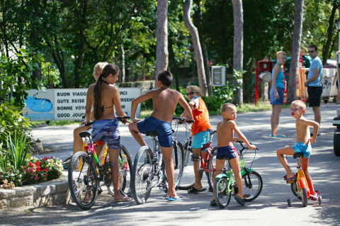 Niños montan en bicicleta y juegan al sol en el Camping Village Mare Pineta en Friuli-Venezia Giulia, Italia.