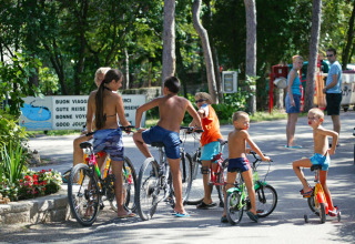 Bambini giocano e vanno in bicicletta al sole al Camping Village Mare Pineta in Friuli-Venezia Giulia, Italia.