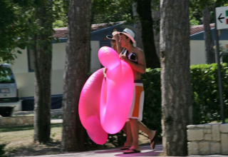 Deux personnes marchent avec une bouée rose au Camping Village Mare Pineta, Friuli-Venezia Giulia, Italie.