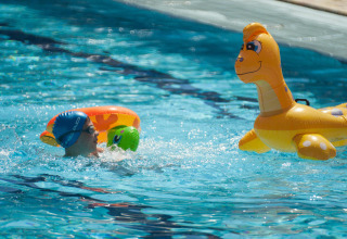 Bambino nuota con ciambella accanto a un dinosauro gonfiabile in piscina al Camping Village Mare Pineta, Italia.