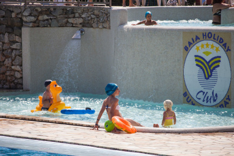 Niños y adultos disfrutan de la piscina en Camping Village Mare Pineta en Friuli-Venezia Giulia, Italia.