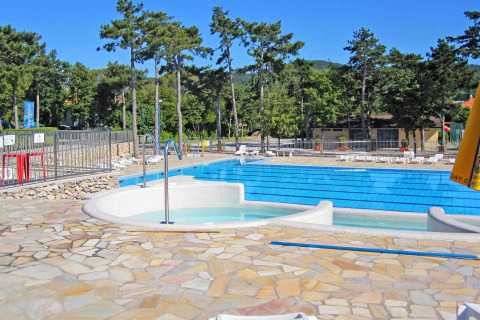 Piscina al aire libre en Camping Village Mare Pineta, rodeada de árboles, tumbonas y paisaje montañoso.