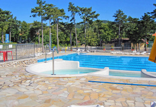 Udendørs swimmingpool ved Camping Village Mare Pineta omgivet af træer, solstole og bjergrig baggrund.
