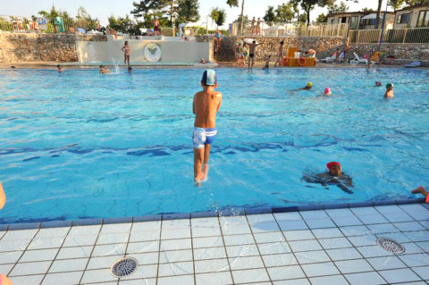 Niños juegan y nadan en la piscina exterior de Camping Village Mare Pineta en Friuli-Venezia Giulia, Italia.