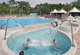 Swimmingpoolområde i Camping Village Mare Pineta, Friuli-Venezia Giulia, Italien med mennesker, liggestole og telte.