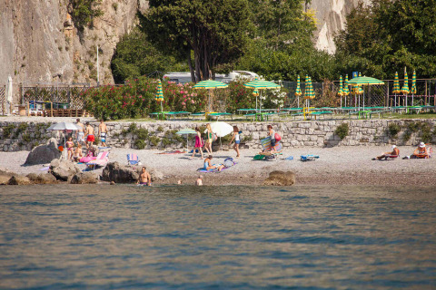 Beach scene at Camping Village Mare Pineta with guests, umbrellas, and rocks in Friuli-Venezia Giulia, Italy.