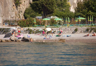 Scena di spiaggia al Camping Village Mare Pineta con ospiti, ombrelloni e rocce in Friuli-Venezia Giulia, Italia.